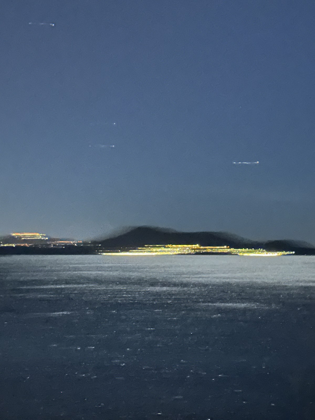 City lights along a dark coastline at night, seen across the water